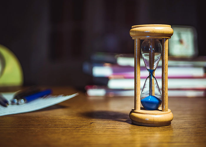 Hourglass with blue sand on wooden table, symbolizing time management life hacks shared by people.