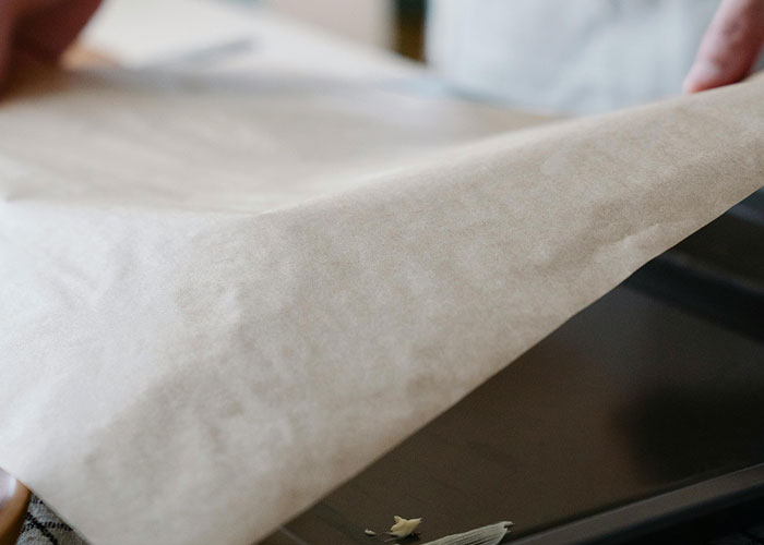 Hands placing parchment paper on a baking tray as a simple genius cleaning hack inspired by laziness.