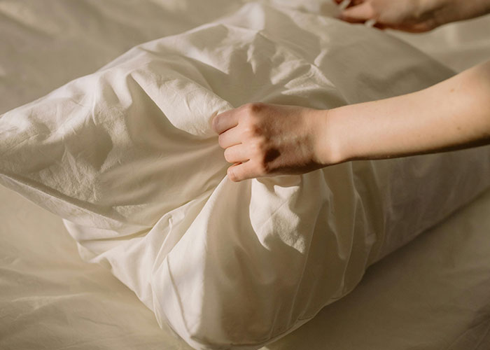 Hands folding a white bedsheet with a life hack technique people are sharing and surprised others don't use.