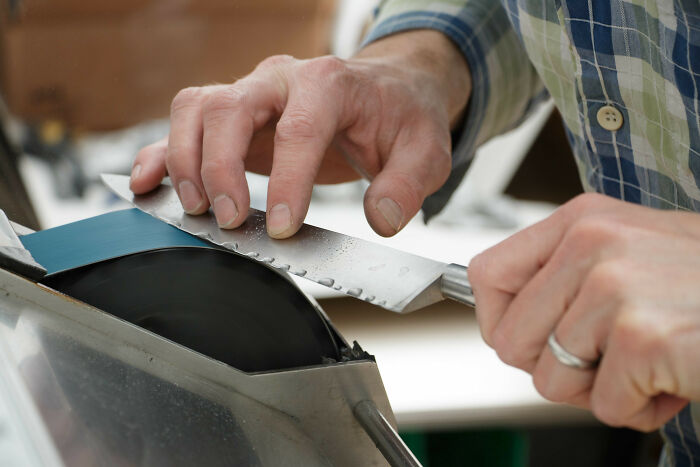 Person sharpening a serrated knife on a rotating grinding wheel to improve kitchen knife sharpness.