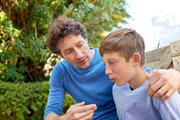 Man comforting sad boy outside, illustrating emotional signs a child was never loved properly in a natural setting.