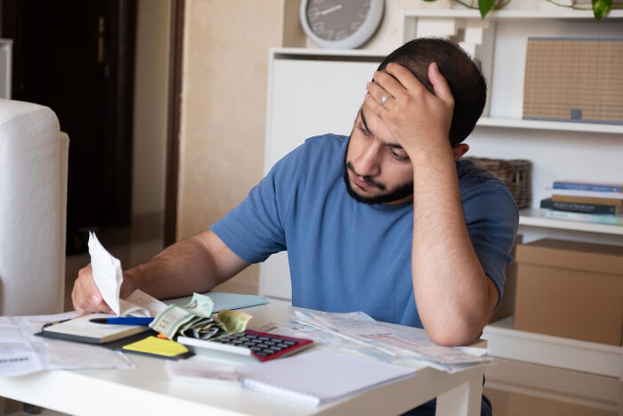 Man stressed while reviewing bills and money at home, illustrating lessons learned from financial mess-ups.