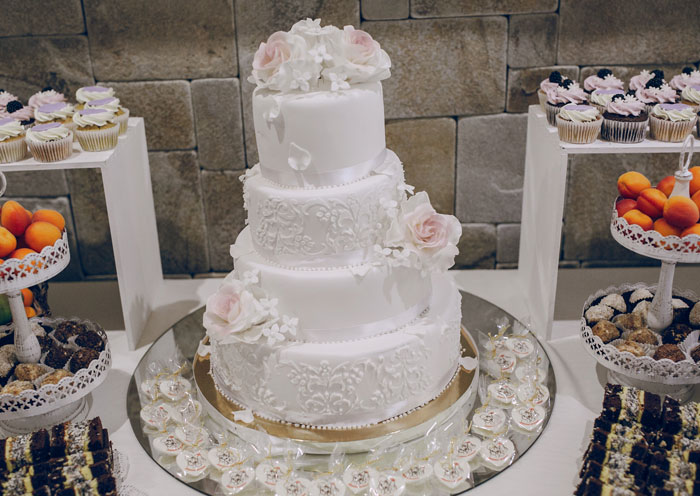 Elegant white wedding cake with floral decorations surrounded by assorted desserts at bride wants honeymoon upgrade event