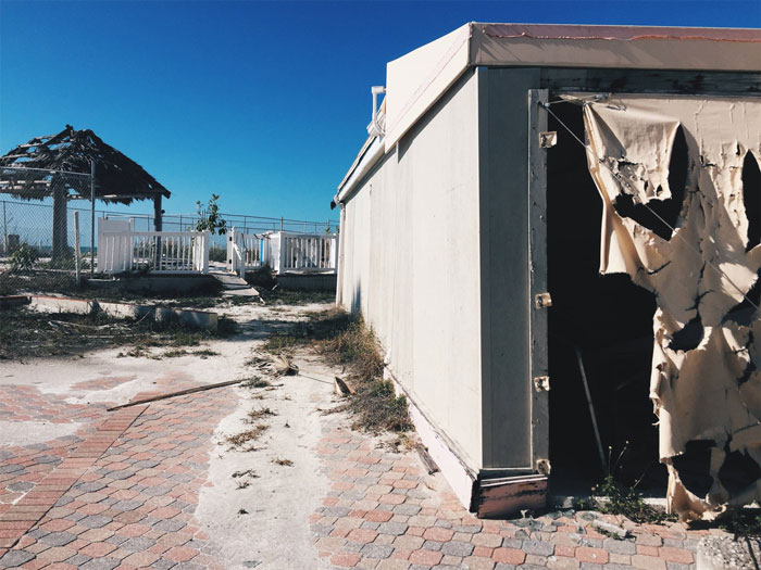 Abandoned urban explorer site with torn building entrance and broken gazebo under clear blue sky during daytime.