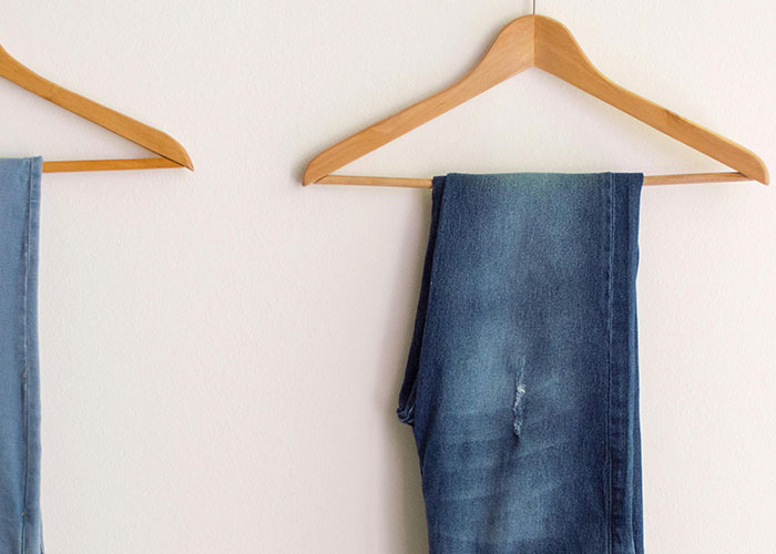 Wooden hangers holding neatly folded jeans against a plain wall, illustrating practical life hacks people share.