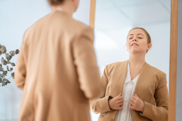 Young woman in a brown blazer looking at her reflection, representing signs a child was never loved properly.