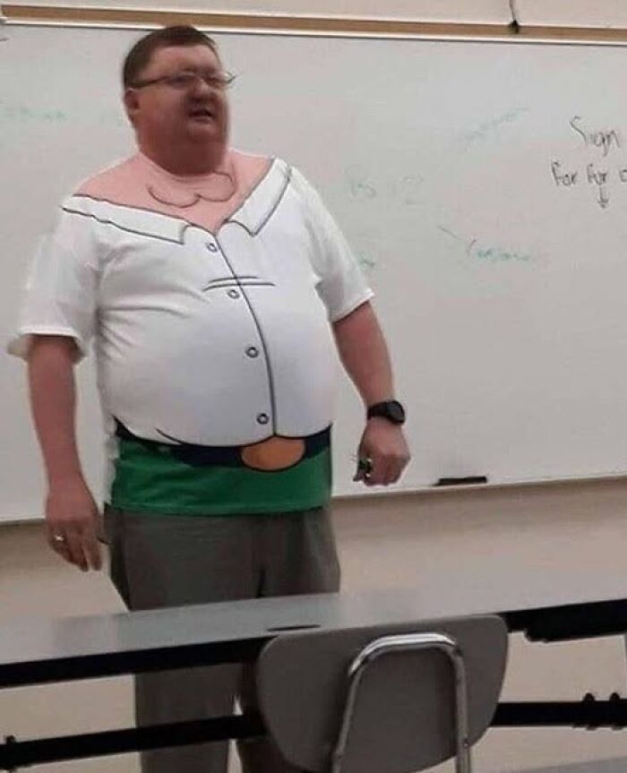 Man wearing a funny cartoon character shirt standing in front of a whiteboard in a classroom setting, funny pics that go hard.