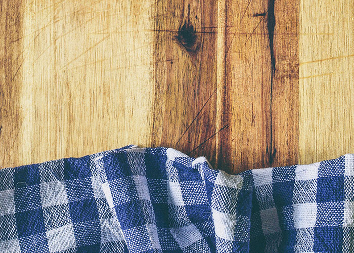 Close-up of a blue and white checkered cloth on a wooden surface showing simple genius cleaning hacks inspired by laziness.