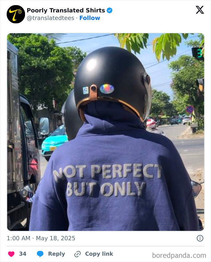 Person wearing a motorcycle helmet and a blue funny English T-shirt with a poorly translated message on a busy street.