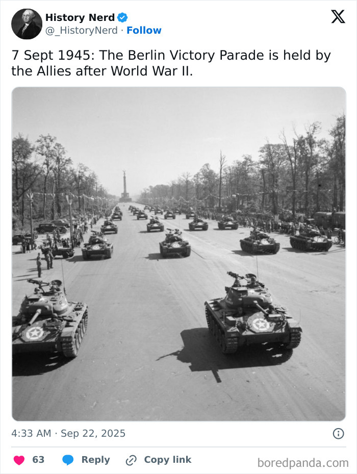 Historic black and white photo of tanks parading down a wide street during a powerful moment in history.