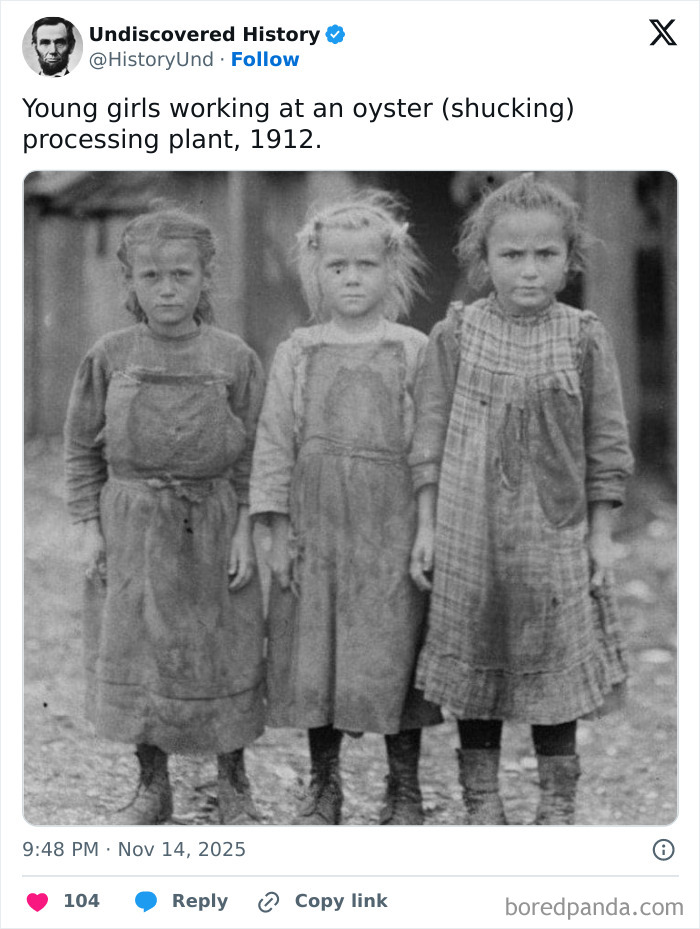 Three young girls in worn clothes working at an oyster shucking plant in 1912, a moment lost to time.