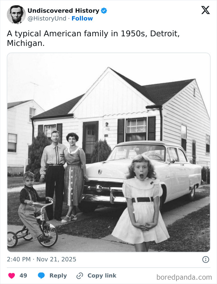 1950s American family posing outside home with vintage car and child on tricycle in a moment lost to time.