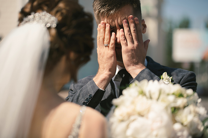 Groom covering face in distress during wedding ceremony as bride stands nearby holding bouquet at outdoor altar. Groom covering face in distress during wedding ceremony as bride stands nearby holding bouquet at outdoor altar.