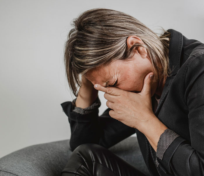 Woman overwhelmed with emotions sitting on a couch, illustrating MIL getting outplayed on vacation with the couple. Woman overwhelmed with emotions sitting on a couch, illustrating MIL getting outplayed on vacation with the couple.