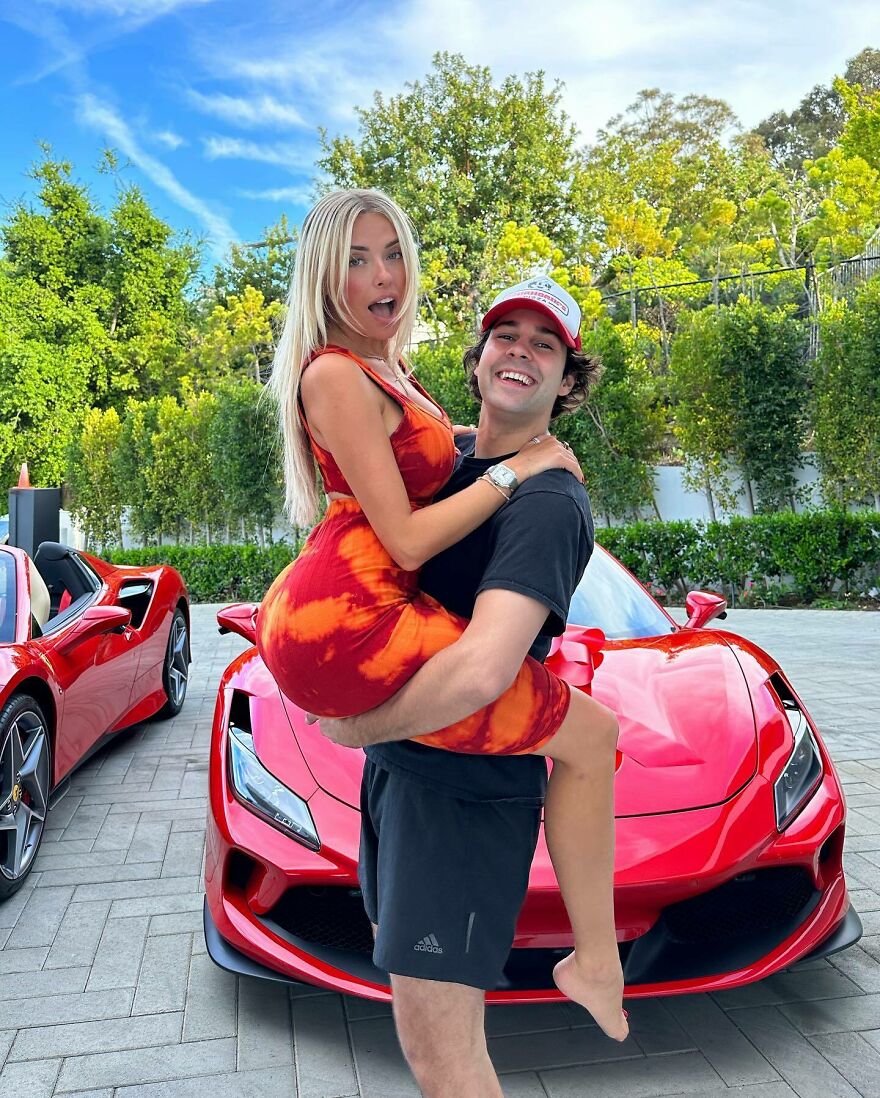Corinna Kopf posing with a man in front of red sports cars, highlighting internet fame and impressive net worth.