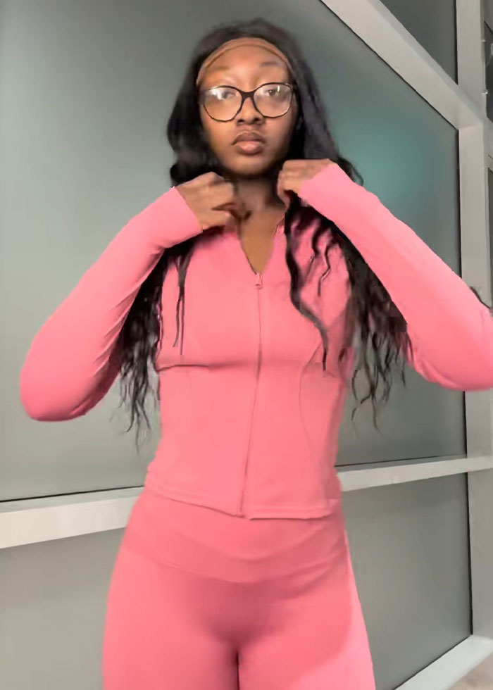 Young woman wearing pink activewear demonstrating trick to hide loose skin on her belly after massive weight loss indoors. Young woman wearing pink activewear demonstrating trick to hide loose skin on her belly after massive weight loss indoors.