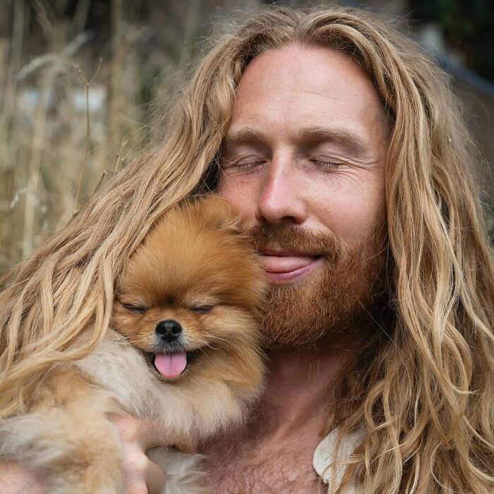 Man with long blonde hair and beard holding fluffy dog with tongue out, showing pets and their humans looking alike.