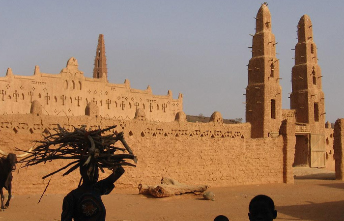 Traditional mud architecture in the poorest country in the world with locals carrying firewood under a clear sky.