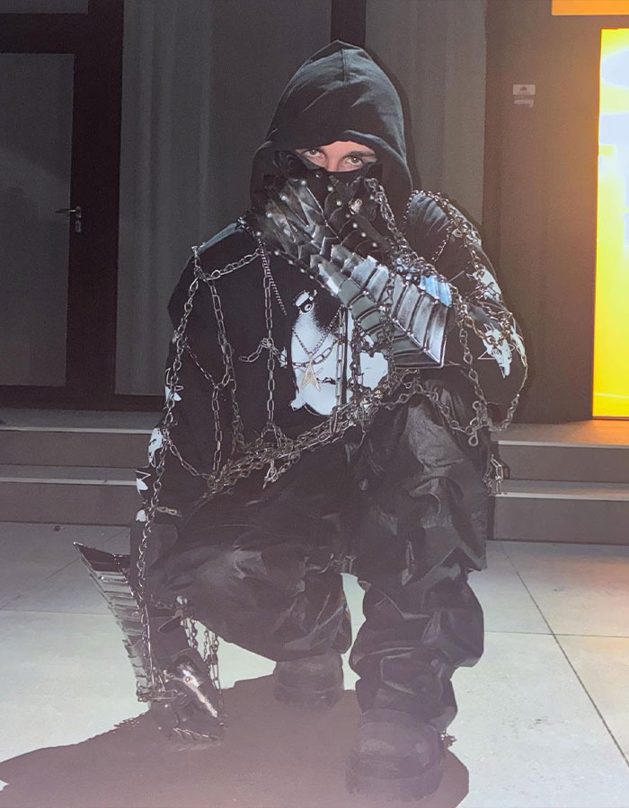 Person in a hooded outfit with chains and metallic gloves posing, fueling fans' theory of Timothée Chalamet as rapper EsDeeKid. Person in a hooded outfit with chains and metallic gloves posing, fueling fans' theory of Timothée Chalamet as rapper EsDeeKid.