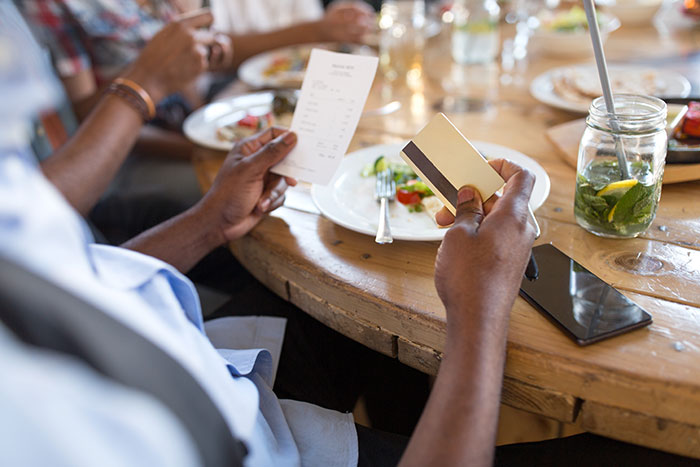 Man holding credit card and receipt at restaurant dinner table while friends eat around him, illustrating taking advantage at dinner. Man holding credit card and receipt at restaurant dinner table while friends eat around him, illustrating taking advantage at dinner.