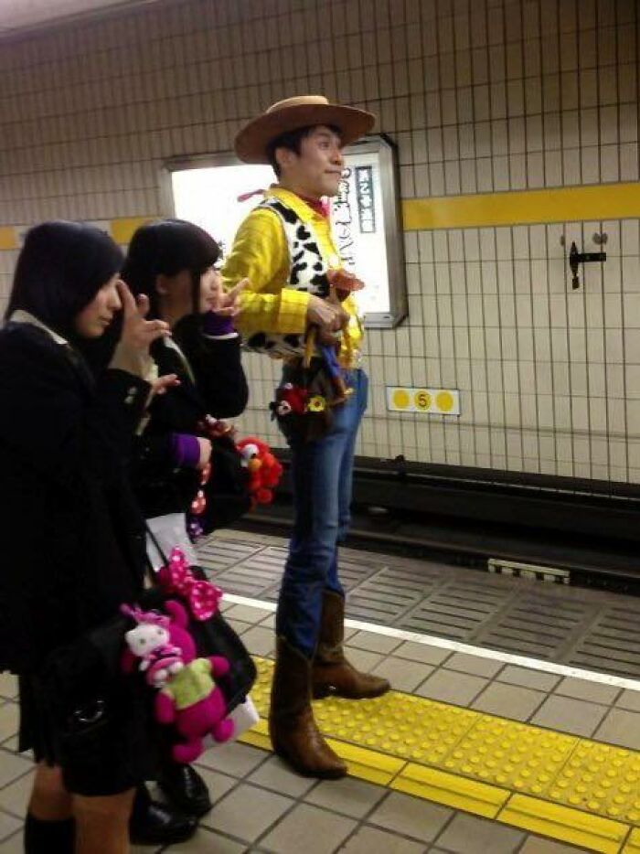 Man dressed as Woody from Toy Story standing on subway platform with two women holding plush toys, a pic that goes hard.