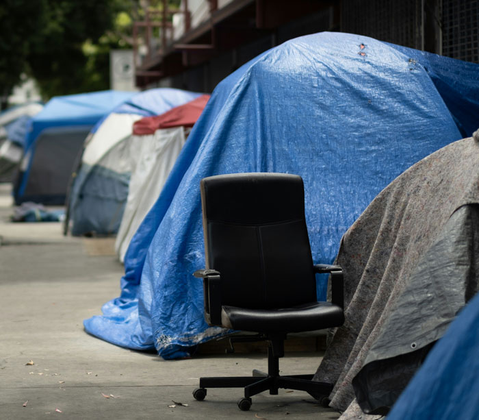Black office chair in front of tents covered with tarps along an urban sidewalk during an eerie urban exploration scene