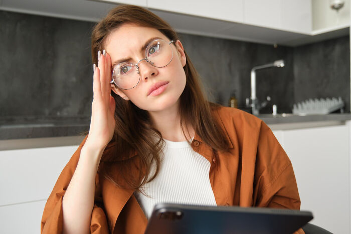 Young woman wearing glasses, looking puzzled while holding a tablet, reflecting on compulsory things being optional.