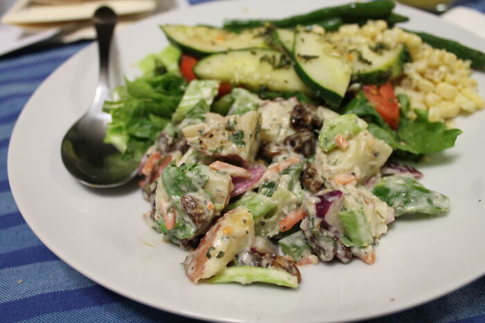 Plate of mixed salad with creamy dressing and grilled vegetables served on a white plate with a spoon nearby.