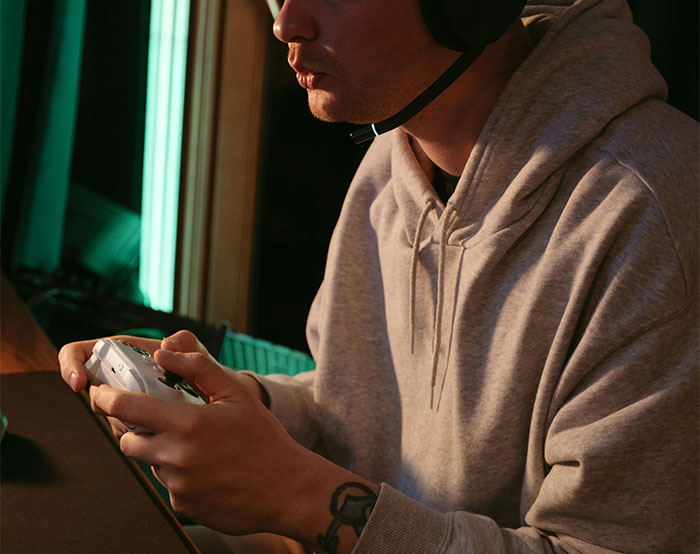 Young man wearing a hoodie and headset playing video games, highlighting entitled parents and autistic brother dynamic.