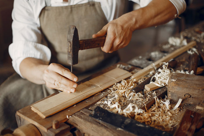 Person crafting wood with hammer and chisel on a wooden workbench covered in wood shavings, family drama concept.