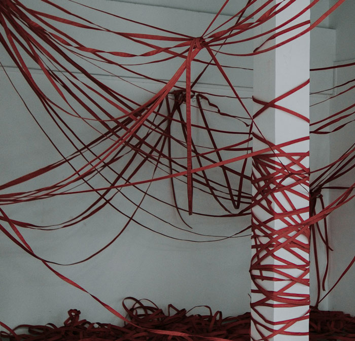 Red ribbons intricately wrapped around a white pillar and ceiling, creating a creepy and terrifying urban exploration scene.