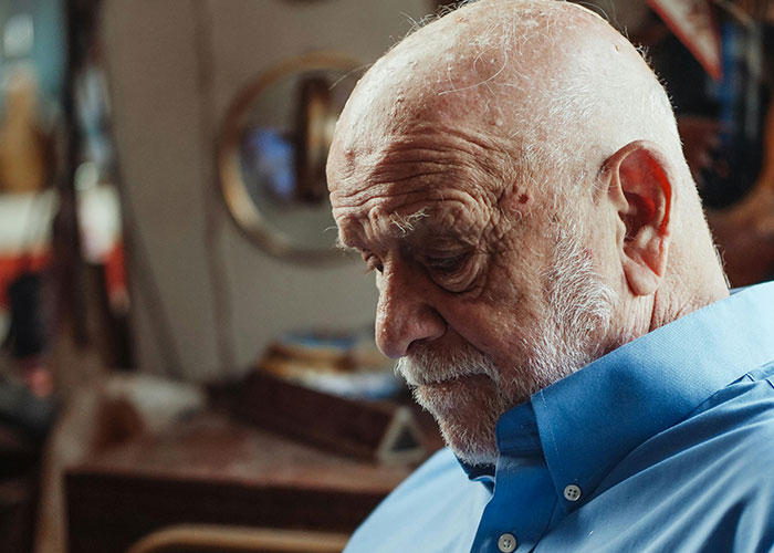 Elderly man in a blue shirt reflects quietly indoors, evoking moments from psychiatric institution workers' unforgettable experiences.