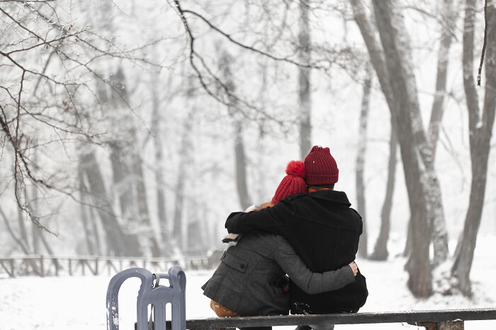 Two people wearing red hats hugging on a bench in a snowy park showing signs a child was never loved properly.