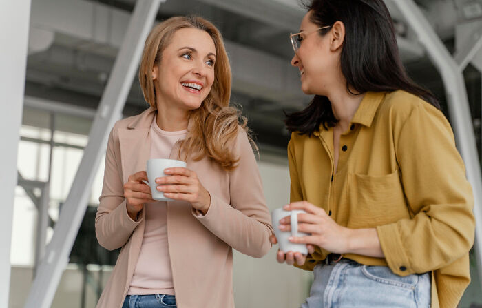 Two women smiling and chatting while holding mugs, illustrating stories of folks realizing compulsory things in life are optional.