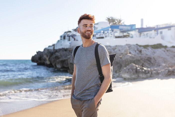 Young man smiling on beach with backpack, symbolizing people who disappeared to start new lives and reveal experiences.