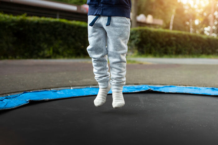 Child in grey sweatpants jumping on a trampoline outdoors, capturing funny and serious moments of raising monsters.