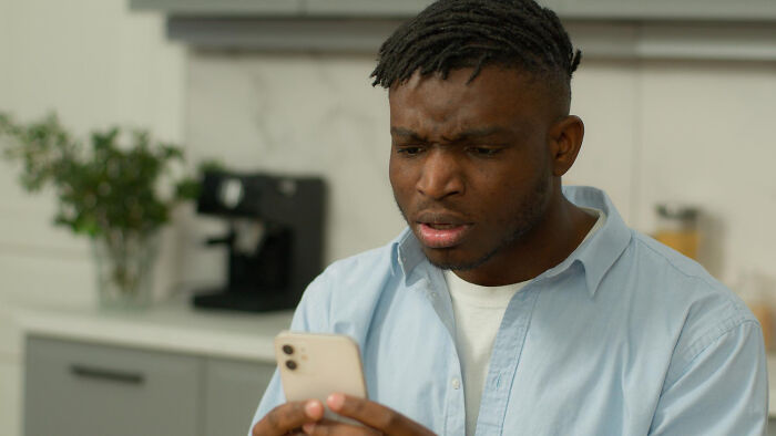 Young man in a kitchen looking concerned at his phone, showing subtle signs they’re cheating in a relationship
