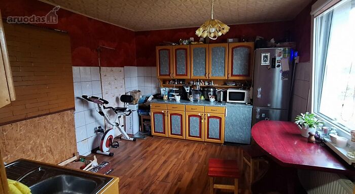 Rustic kitchen interior with wooden cabinets, red walls, exercise bike, and table in wild real estate listings photo.