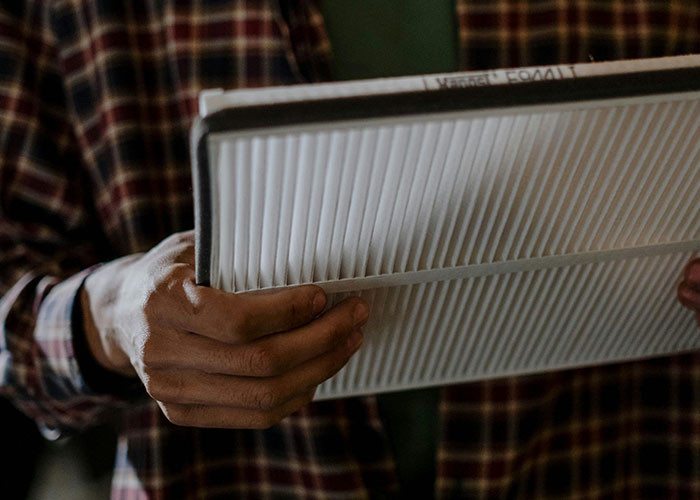 Person holding a white pleated air filter demonstrating a genius cleaning hack inspired by laziness.