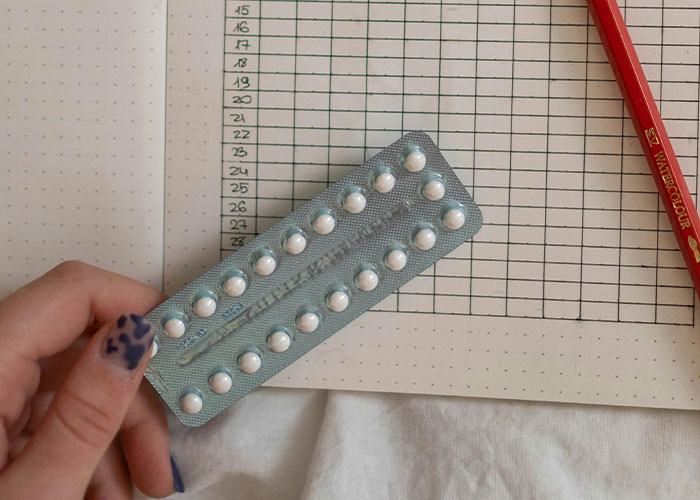 Hand holding a blister pack of pills over a habit tracker, illustrating life hacks for daily organization.