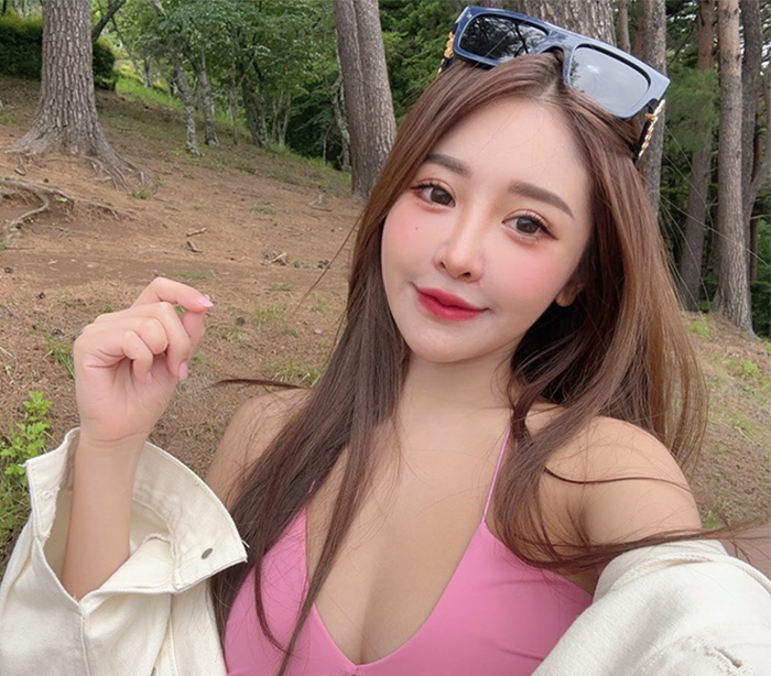 Provocative influencer wearing pink top and sunglasses posing outdoors with trees and dirt background. Provocative influencer wearing pink top and sunglasses posing outdoors with trees and dirt background.