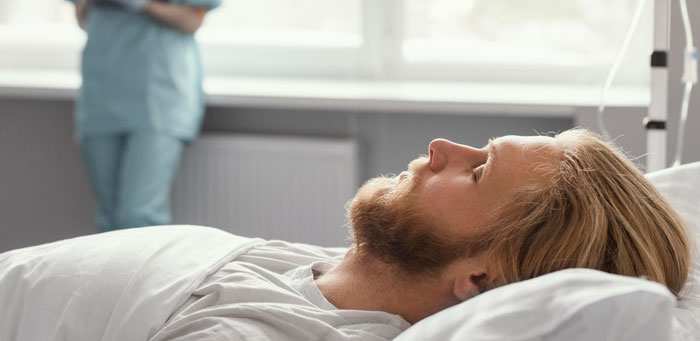 A young man lying in a hospital bed with a nurse standing nearby, capturing intense family drama moments.