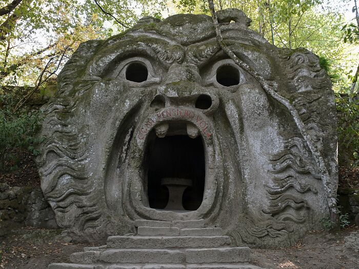 Stone sculpture of a giant face with an open mouth entrance surrounded by trees, a spectacular travel attraction.