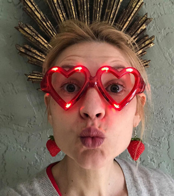 Woman with quivering chin wearing red heart-shaped light-up glasses and strawberry earrings in a playful close-up portrait. Woman with quivering chin wearing red heart-shaped light-up glasses and strawberry earrings in a playful close-up portrait.