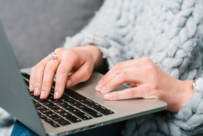 Close-up of a woman typing on a laptop while wearing a cozy gray sweater, illustrating MIL coming with couple on vacation story. Close-up of a woman typing on a laptop while wearing a cozy gray sweater, illustrating MIL coming with couple on vacation story.