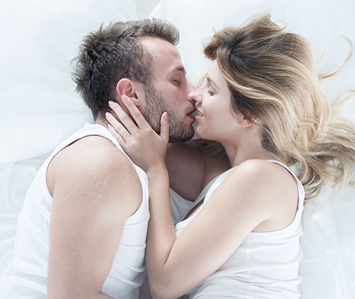 Couple in white tank tops embracing intimately in bed, highlighting emotions related to cheating husband and inspiring update.