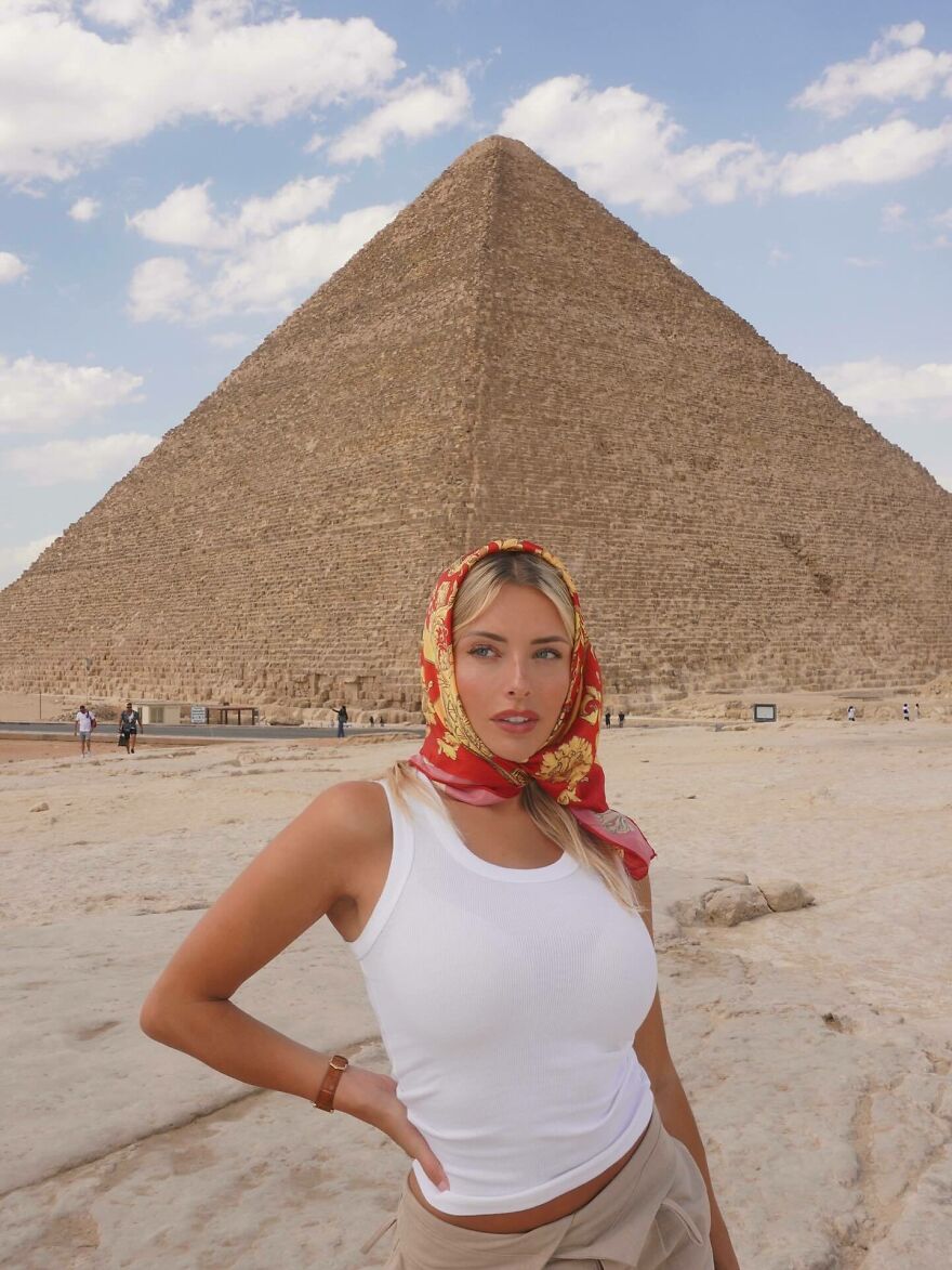 Corinna Kopf posing near the Pyramid of Giza wearing a white tank top and red scarf, showcasing internet fame and net worth.
