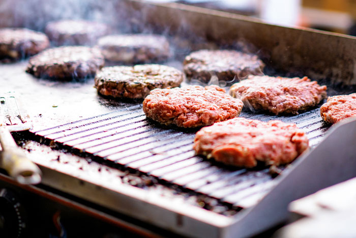 Raw and cooked burger patties sizzling on a grill, capturing the glorious moment of instant karma in cooking.