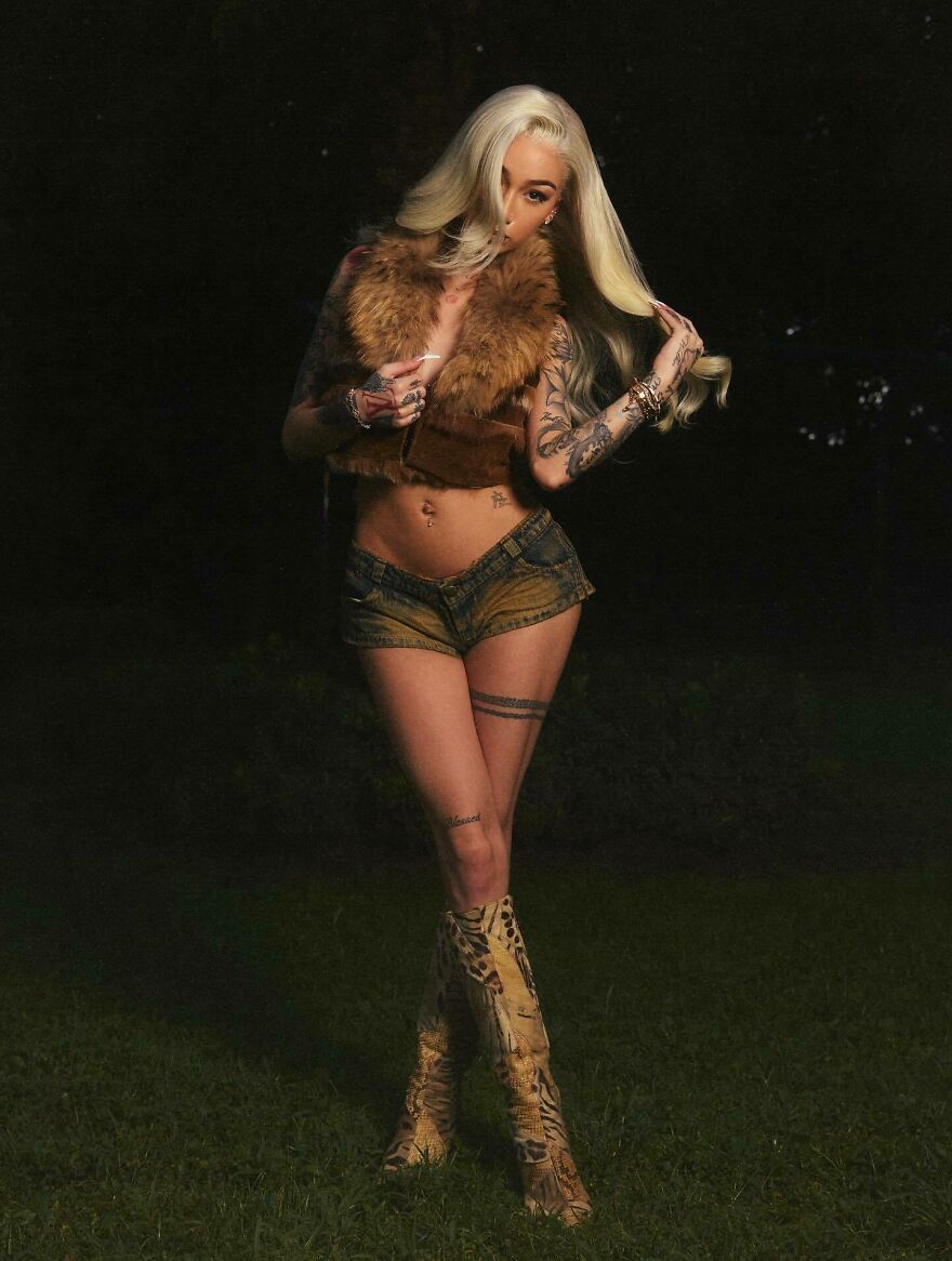 Bhad Bhabie posing outdoors at night, wearing a fur vest, denim shorts, and patterned boots showing a confident style. Bhad Bhabie posing outdoors at night, wearing a fur vest, denim shorts, and patterned boots showing a confident style.