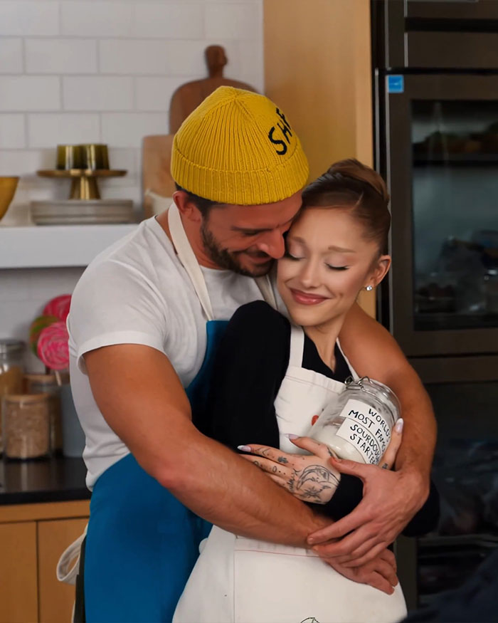 Ariana Grande and Jonathan Bailey hugging in a kitchen, sharing a warm and intimate moment while baking together. Ariana Grande and Jonathan Bailey hugging in a kitchen, sharing a warm and intimate moment while baking together.